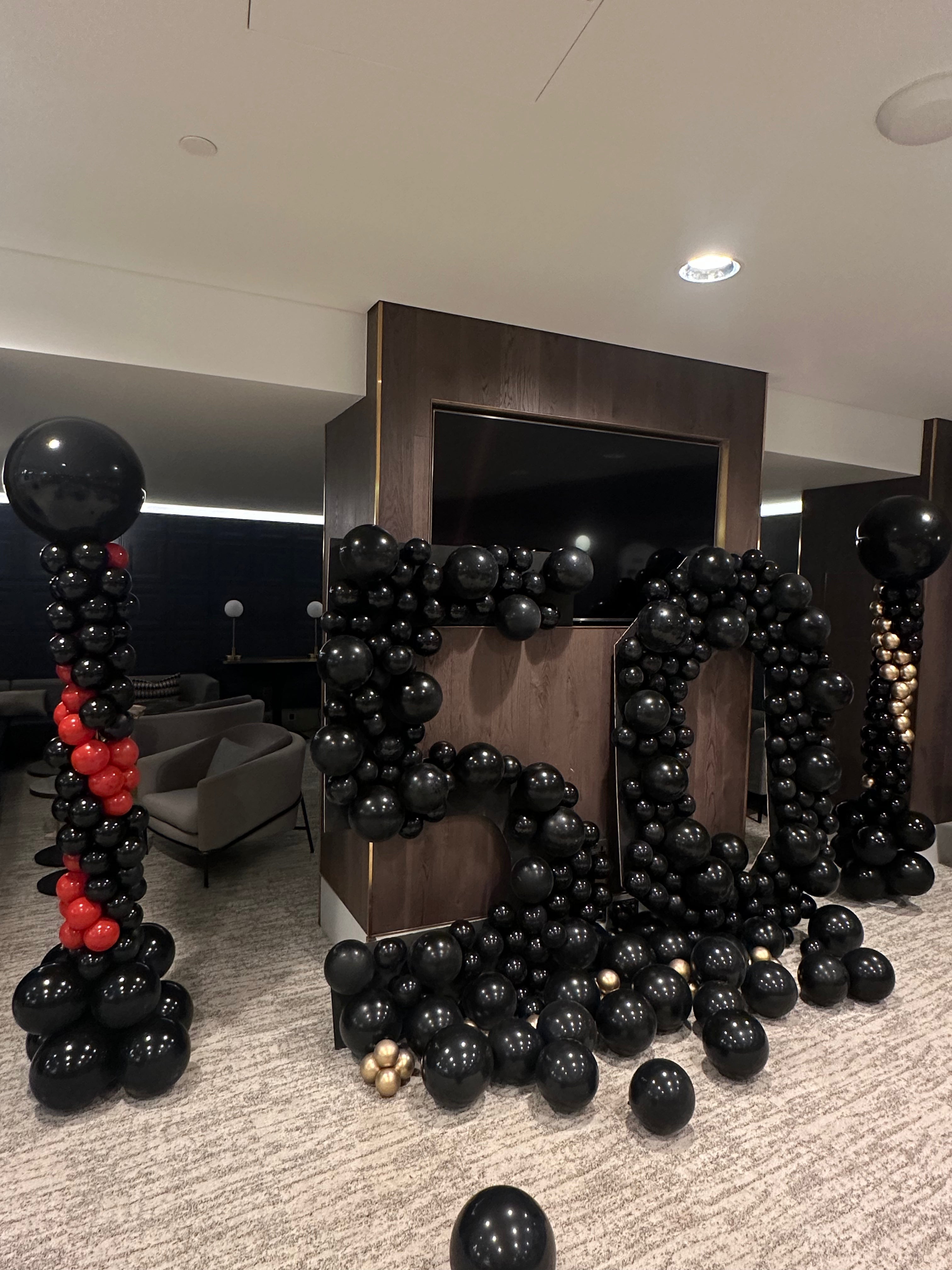 A large black balloon garland for 50 Cent displayed in a modern indoor event space at Tottenham Hotspur, with matching balloon columns on both sides and scattered black balloons on the carpeted floor.