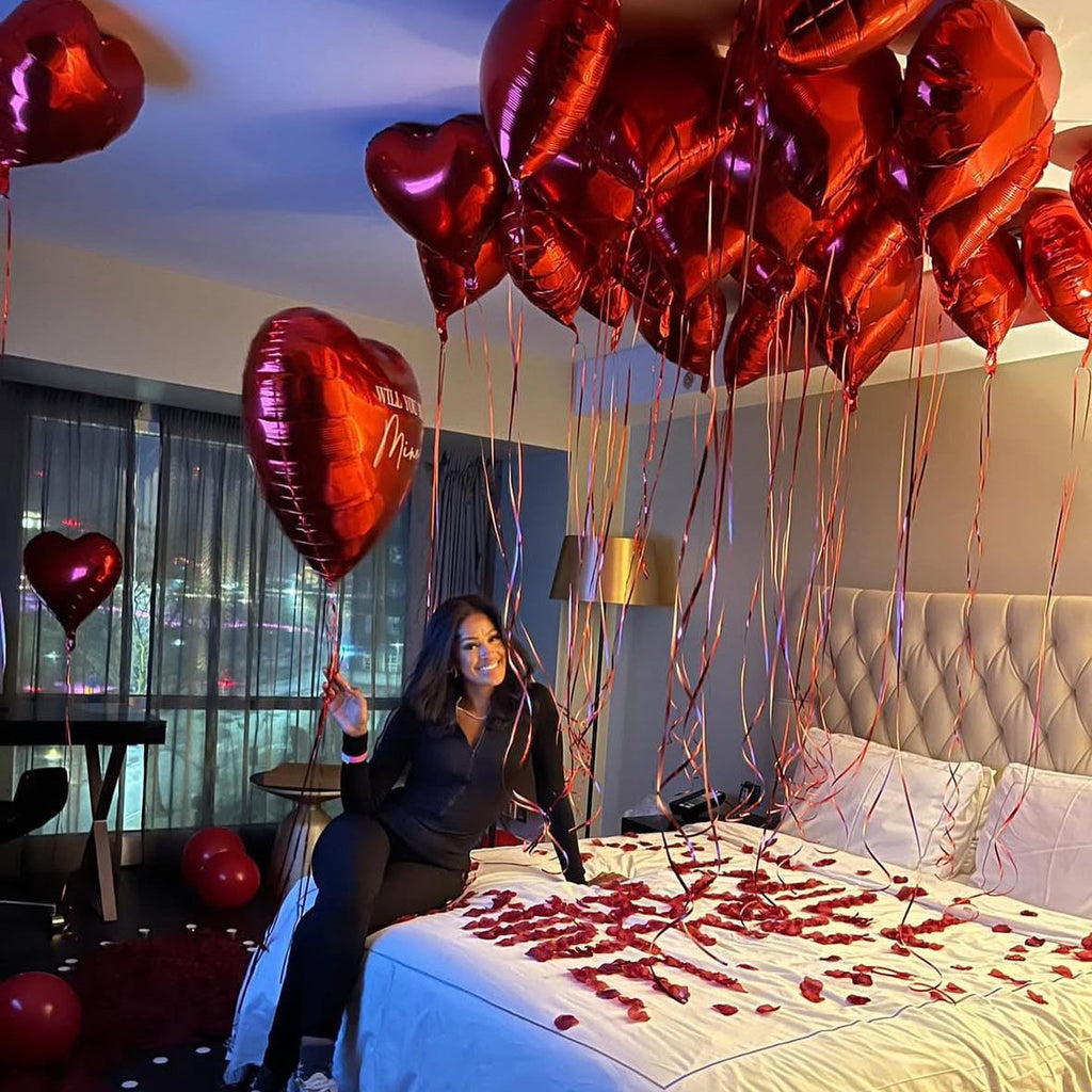 Hotel decor for girlfriend proposal with red heart balloons and petals
